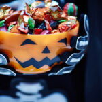 Bowl with candies decorated as Jack O'lantern in the hands of Halloween character